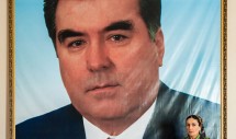Title: Woman with portrait of Tajik President, Dushanbe, August 19, 2010. Caption: A woman who works in the Tajikistan National Museum stands in front of a large portrait photograph of the Tajik president Emomalii Rahmon on August 19, 2010. One might quickly interpret this image to symbolize the power of patriarchy and of political hegemony. Both are pervasive in Central Asia. Yet this particular woman was happy to pose for a photo with her President -- perhaps out of sharing a moment with a stranger, or out of duty towards a guest. She may have also felt esteem for her President. Ethnography could provide a glimpse of how she has come to understand and act on what power she does have, potentially initiating conversations on the quality of her social relationships.