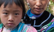 Title: Mother and dauther, Hani people, Zuofu Village in Yunnan, China, February 1, 2011 Caption: The trans-national people generally known as Akha reside as separate groups in five different countries in Asia. In China, they are know as the Hani minority, inhabiting the southern part of Yunnan. The Hani speak a variety of dialects related to the Tibeto-Burman language group, their written system was developed in 1957 based on the roman alphabet. Hani clothing usually includes black and homespun dark blue cloth, with silver adornments being used by both men and women. Different female hats are used at different ages and vary from community to community. In the poor village of Zuofu, the silver coins and ornaments are rare. The Hani are one of the poorest minorities in China.  