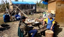 Title: Grandma Maggie's Back Yard (May 2012) Caption: What appears to the untrained eye as a cluttered yard forms the basis for Maggie Roberts' subsistence lifestyle in Venetie, Alaska. Here she is interviewed by her grandson, Kenneth Frank, as part of our NSF-funded project to document Gwich'in Caribou Anatomy and Cultural Ecology. Gwich'in is an endangered language spoken in northeast Alaska and Northwest Canada.  