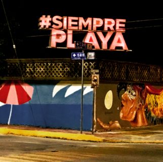 An electric sign on a darkened street corner reads "#SiemprePlaya."