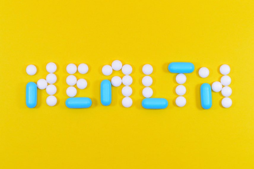 Blue and white pills spell out the word "Health" in all caps.
