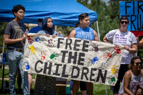 Four people hold a banner that reads "free the children" and has mulicolored palm prints on it.