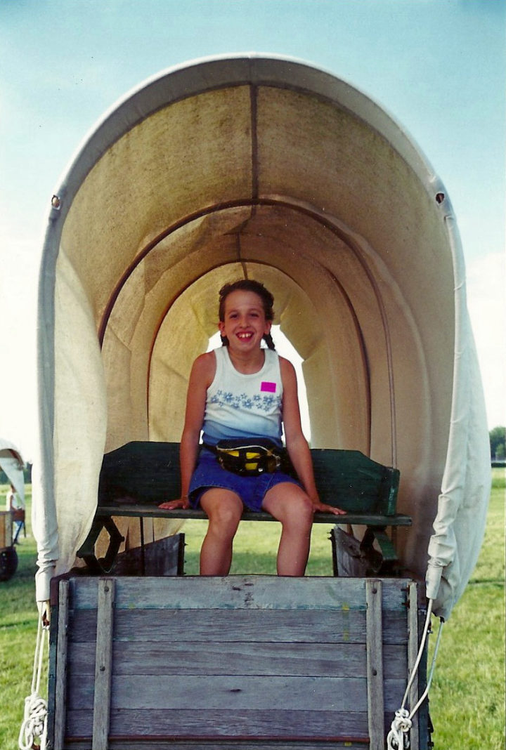 Laura Heath-Stout is portrayed as a child in this photograph, seating on an old wagon, looking happy.