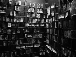 A black and white photo of a room where people hang photographs of their loved ones. There are over 12 rows of photos, from floor to ceiling, clipped to strings that run from wall to wall.