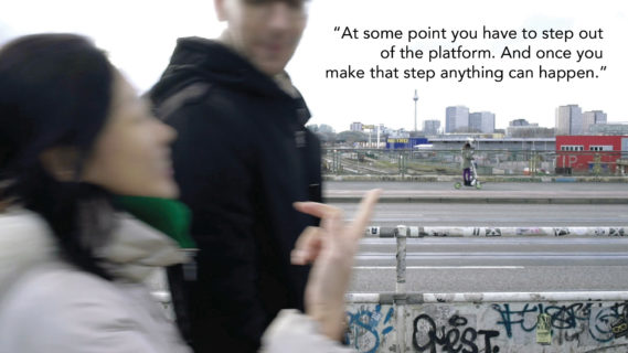 A woman and man walk along the side of a highway in the middle of a conversation. The text in the photo, a quote from an interlocutor, reads: "At some point you have to step out of the platform. And once you make that step, anything can happen."