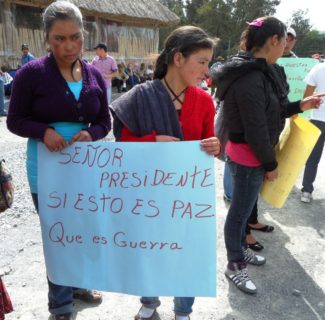 Two young women hold a sign that reads, "Senor presidente, si esto es paz, que es guerra?"