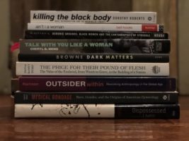 Stack of books lying on a table written by black women including Dorothy Roberts, Bell Hooks and Cheryl D. Hicks
