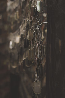 Tens if not hundreds of dogtags hang from small hooks on a wall