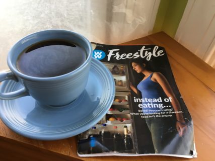 Close up of a cup of coffee and a weight loss brochure, which shows a woman looking into an open refrigerator.