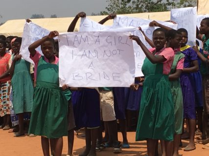 Two girls in identical school uniforms hold up a sign that reads "I am a girl. I am not a bride."