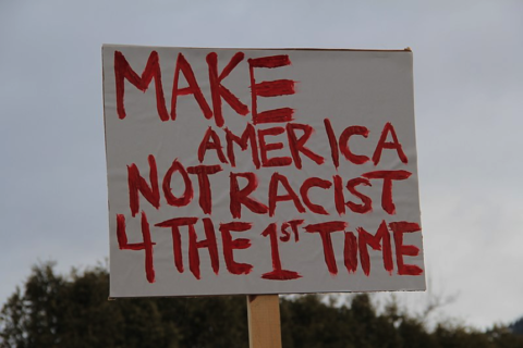 Sign with handpainted letters reads 'Make America Not Racist 4 the 1st Time'.