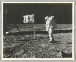 Astronaut Buzz Aldrin next to US flag on lunar landscape.