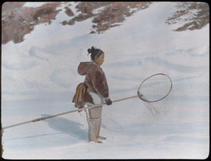 A woman dressed in furs stands on snow with her net in hand.