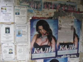 A photo of Bulgarian nekrologs on a wall with other postings nearby, most noticeably an upcoming performance by a female singer.