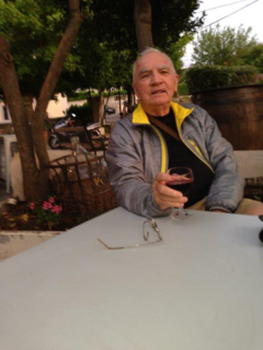 Photo of William P. Mitchell sitting at a patio table with a full glass of wine in his hand.