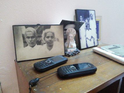 Two mobile phones sit atop a side table in front of framed pictures of elder family members.