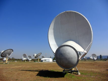 A field of satellites dot an arid field. The sky above is clear.