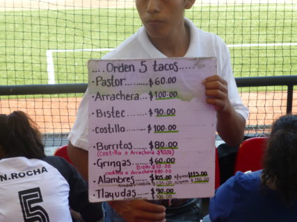 Concession vendor holds a hand-written menu of popular Mexican street foods.