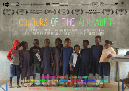 Ten children stand in front of a chalkboard; some hold hands and look at each other, others look at the camera. Atop the photo is the movie title "Colours of the Alphabet" and other text detailing the awards and crew associated with the movie.