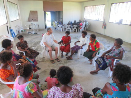 A photo of a large room with two separate circles of chairs with roughly eleven people sitting in them and talking.