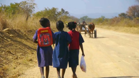 A photo of three children from behind walking down a dirt road.