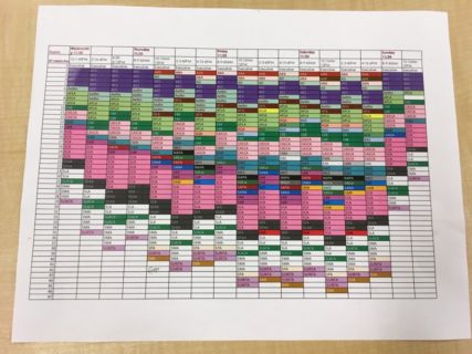 A piece of paper covered with a calendar grid of days and times. The individual time slots are marked with a range of colors.