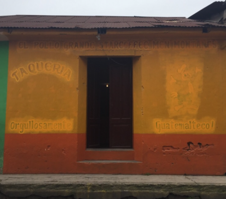 A yellow and red painted adobe building with the faded sign of a taco restaurant.