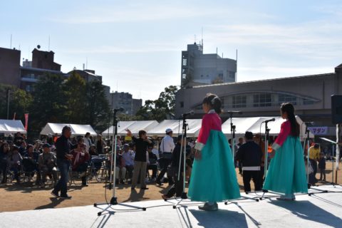 A photo of two Korean schoolgirls in traditional Korean costumes singing on an open-air stage at an intercultural event.
