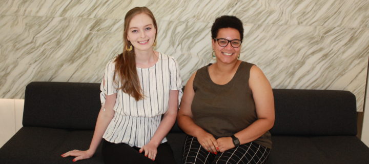 Two women sit side by side smiling for the camera