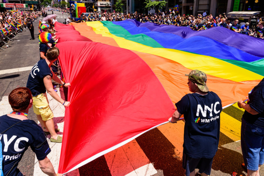 Photograph of multiple people holding an oversized rainbow flag