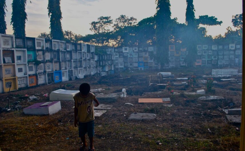 Photograph of a cemetery with young child in foreground and smoke in the air.