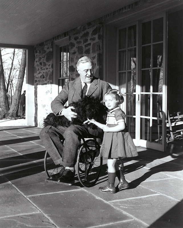 Black and white photograph of a young girl and a man in a wheelchair holding a dog