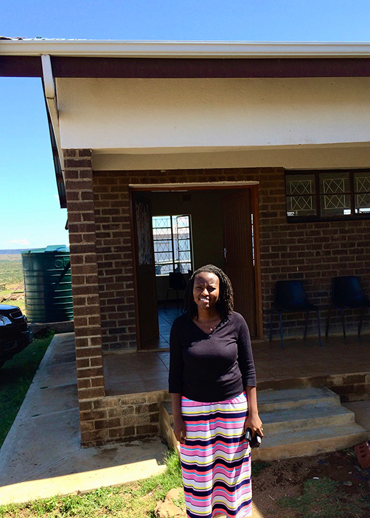 Photograph of a person standing in front of a one-story brick building.
