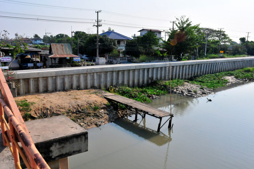 Photograph of a landscape, including a body of water, wall, and buildings.