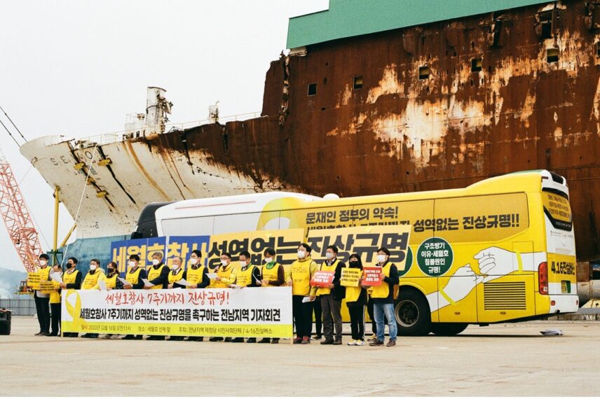 A group of people standing in front of a yellow bus and a rusty ferry.