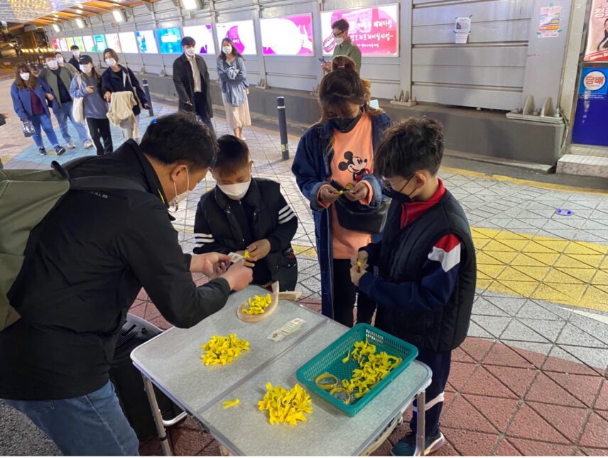 A man hands small yellow ribbons to people at a table in a busy street.