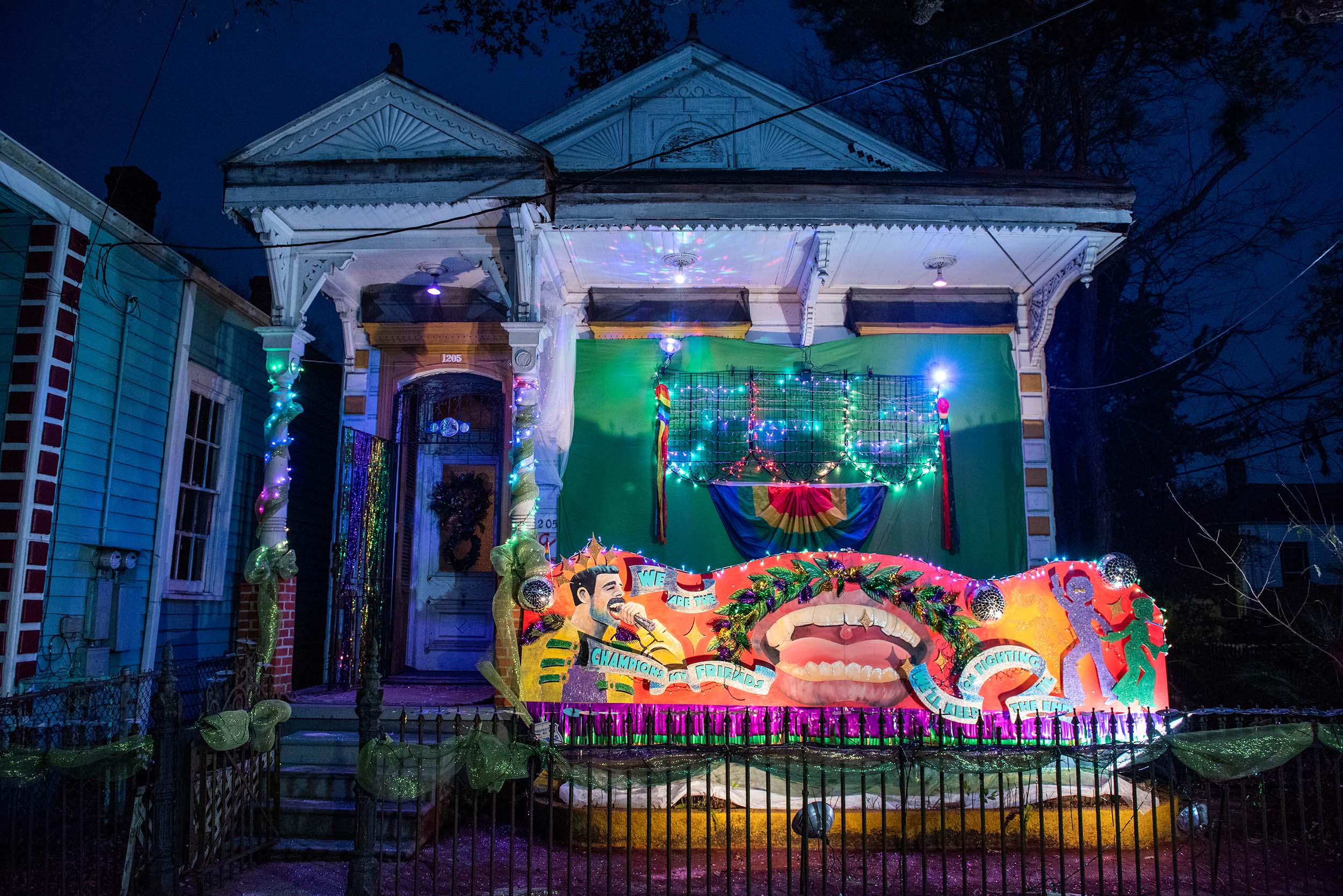 Photo of a housefront at night, lights strung around columns and a mural illuminated