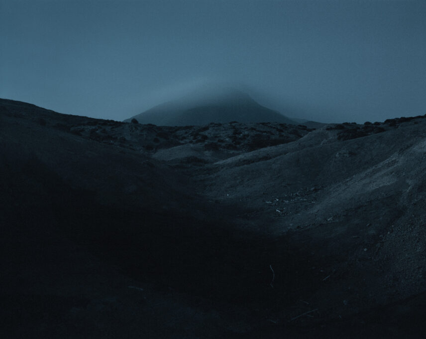 Photograph taken of a landscape seemingly from inside a depression in the ground, all in shades of blue and grey.