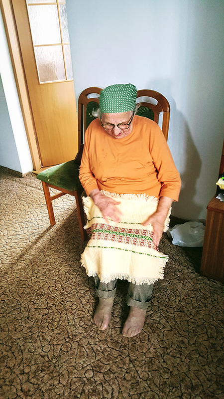 Photograph of an elderly woman sitting in a chair holding a piece of fabric in her lap