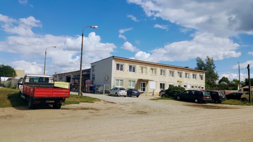Photograph of a worn out building at the centre of the photograph, blue sky and white clouds above it, red van on the side