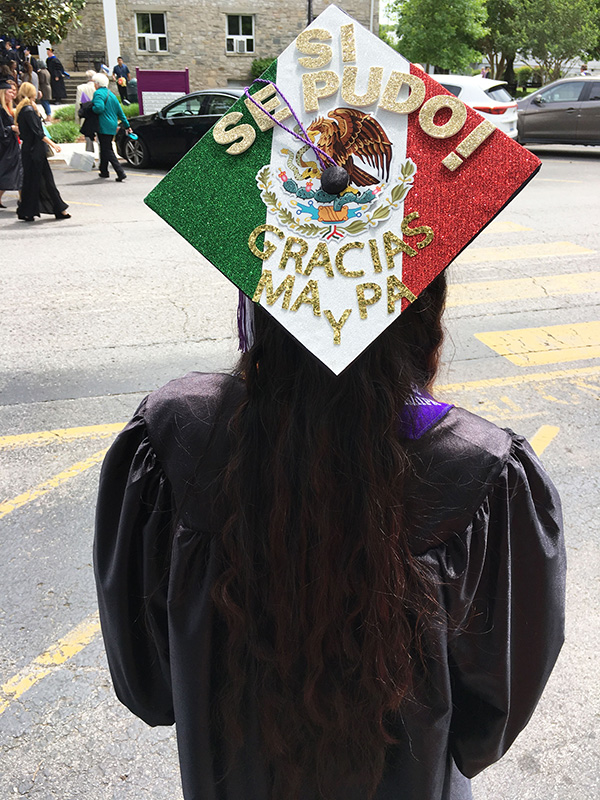 Photograph of a person in graduation cap and gown from the back, displaying their decorated cap prominently
