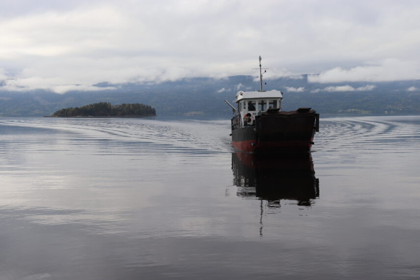 Photograph of a small ferry in front of an island in a Norwegian fjord.