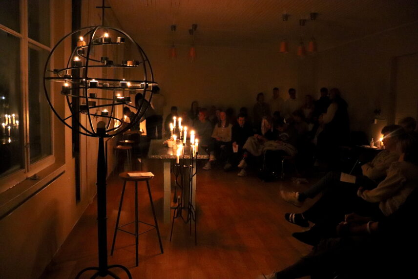 Photograph of students seated around a simple altar in a small room lit by candlelight.