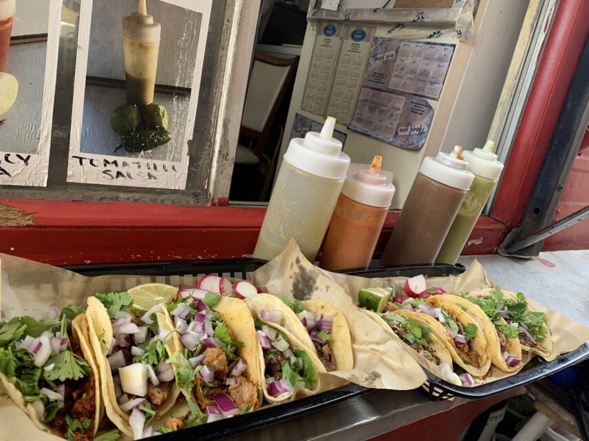 An assortment of tacos placed on the sitting ledge in front of the truck’s window. The tacos contain meat, chopped red onion and cilantro and behind them are the four salsas in squeeze bottles provided by the truck.