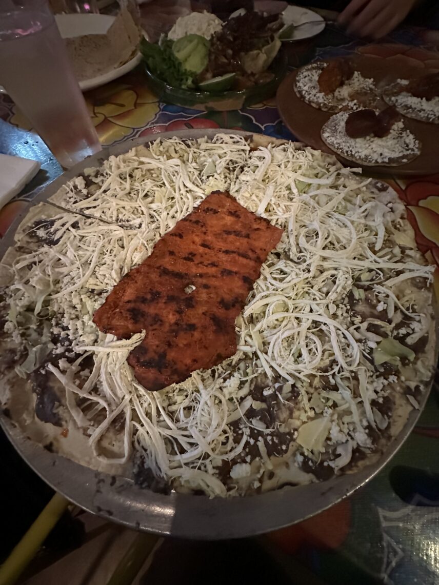 A tlayuda served open-faced like a pizza, this one is topped with black beans, quesillo cheese, cabbage and Cecina, or Oaxacan-style thin sliced pork.
