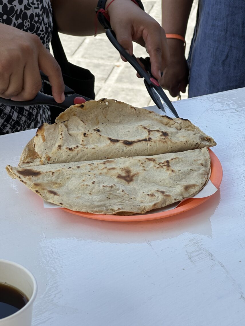 Two closed quesadillas being readied by the attendant for cutting and serving. These were made on an outdoor griddle in Oaxacan City: one contained mole Amarillo (yellow mole sauce) and the other contained squash blossoms and cheese, or in Spanish, flor de calabaze y quesillo.