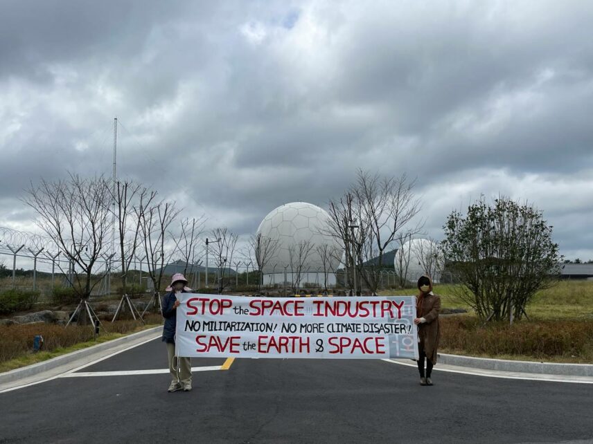 Two activists hold a banner that says "Stop Space Industry"