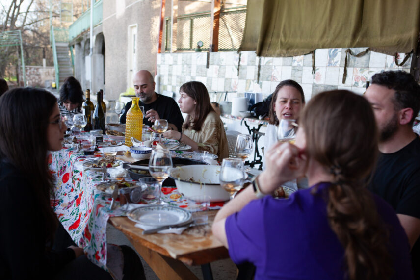 People sit at a table filled with food and wine.