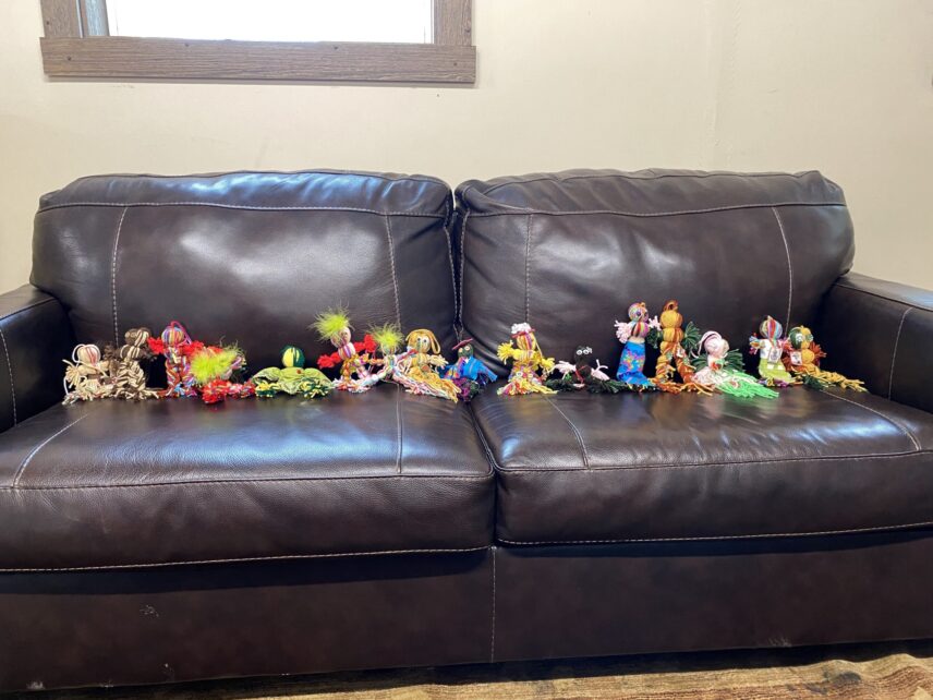 A set of dolls made by the Migrant Lives and Labor in the Upper Valley students line a brown leather couch. The dolls are placed to mimic sitting.
