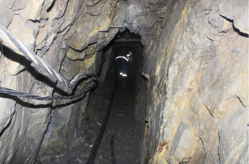 A miner walking slightly crouched through a narrow section of a mining facility.